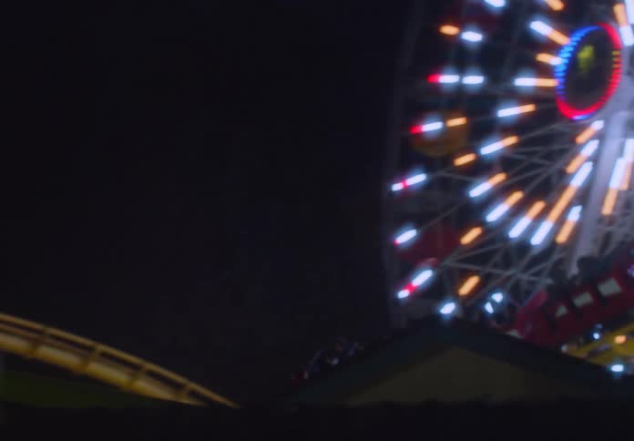 People ride on a roller coaster near the ferris wheel at night