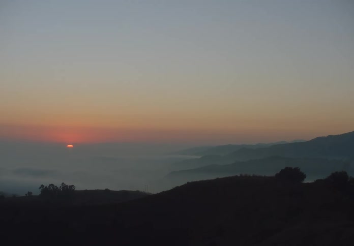 Hint of sun sits on the horizon as fog fills a valley surrounded by mountains