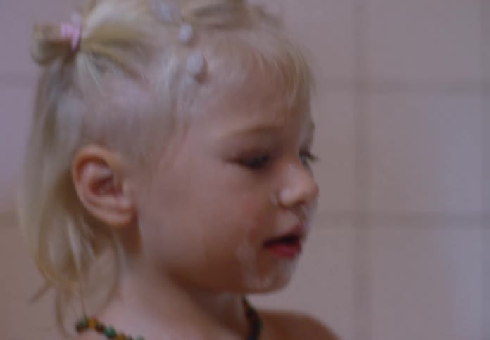 Woman blows soap suds from her palm towards a little girl in the bathtub