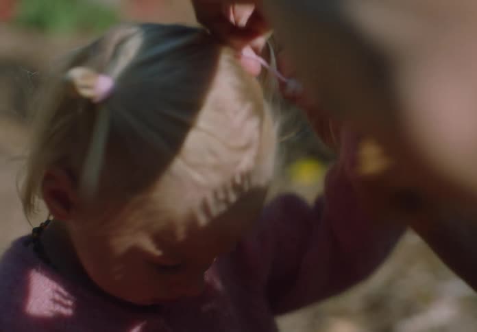 Mother styles the hair of her daughter while outdoors on an autumn day