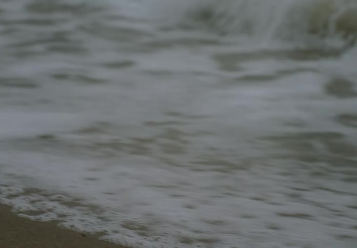 Foaming waves roll into shore and over the sand on the beach