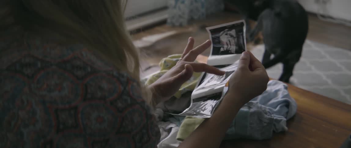 lifestyle footage of a pregnant woman reviewing ultrasound pictures in a living space.