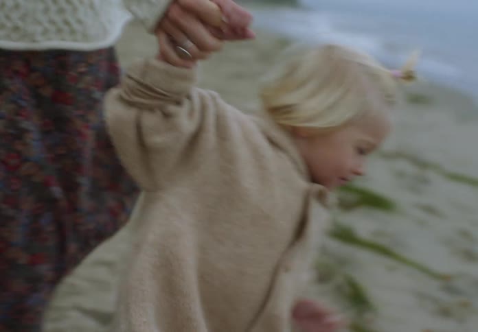 Woman holds the hand of her little girl as they walk barefoot on the beach