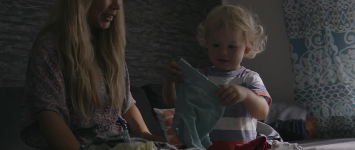 Mother and toddler boy discussing laundry items together in a bright, sunny home.