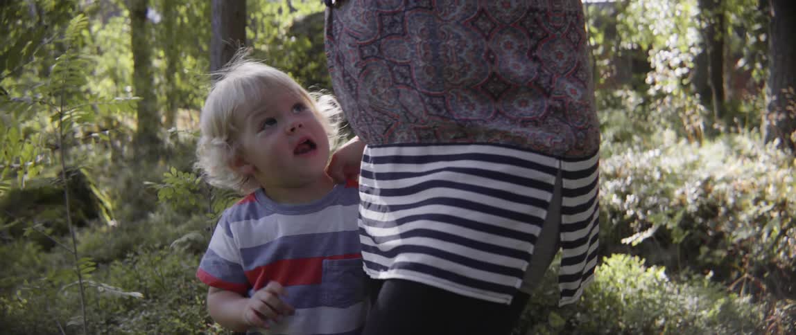 Happy toddler boy looking up at his mother during a playful outdoor afternoon stroll.