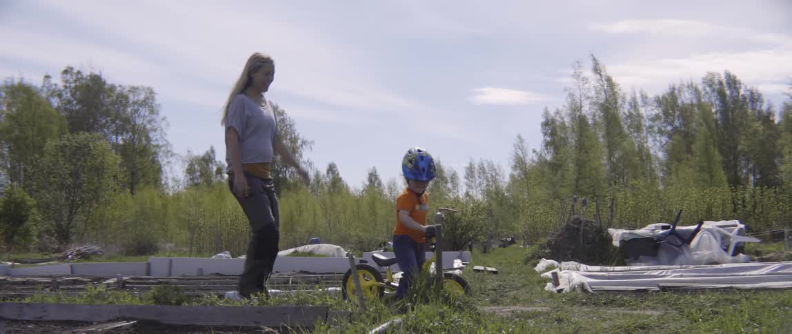 Mother encouraging her young son while he practices riding a bike on a paved trail.