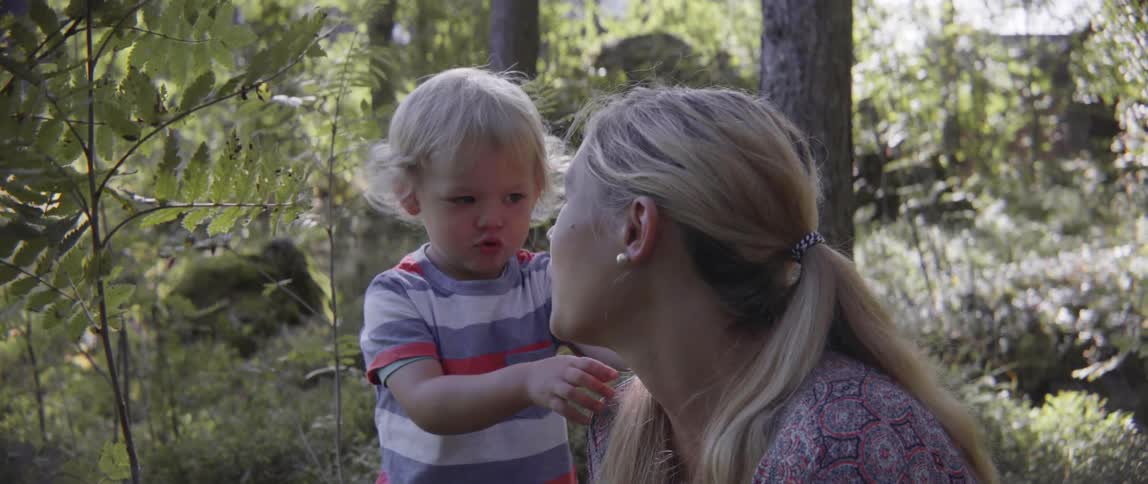 A woman and young boy sit together in the woods having a conversation.