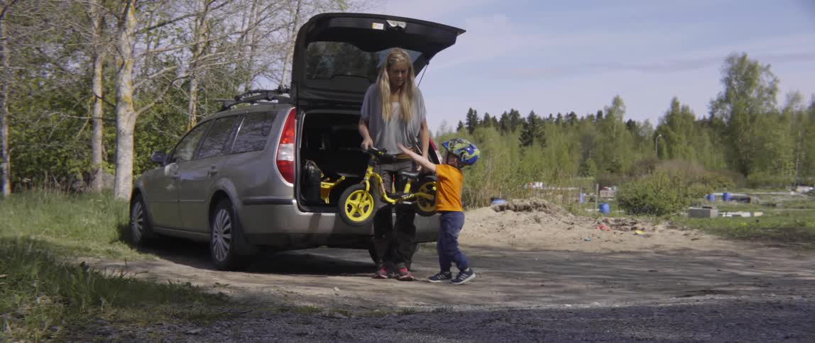 Woman takes bicycle out of car and gives it to little boy wearing helmet