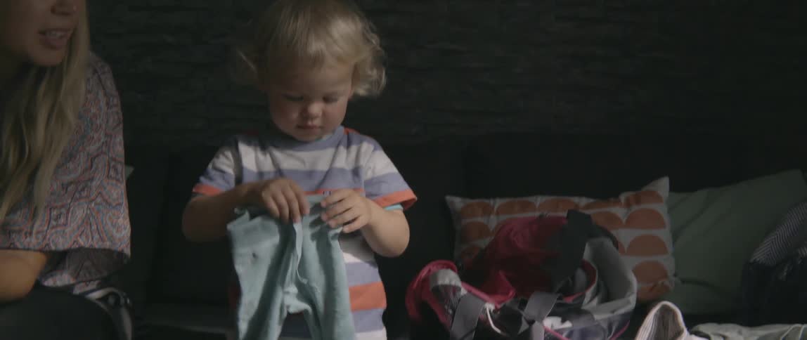 Small child playing with laundry while sitting on the floor by a warm fireplace.