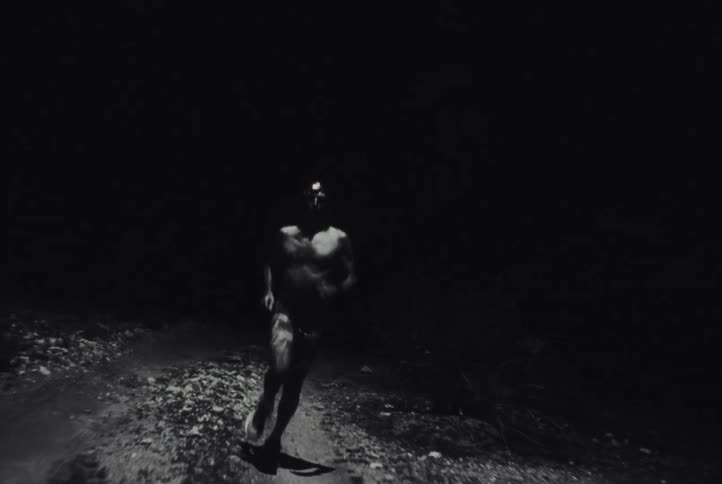 Bare chested man runs along a dirt road at night