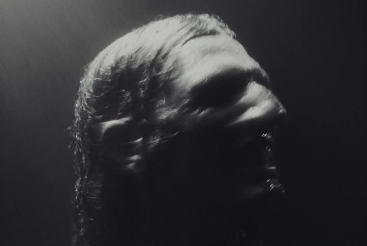 A close up blurred blackandwhite image captures a person yelling and clutching their head illuminated by dramatic lighting that emphasizes motion and emotion