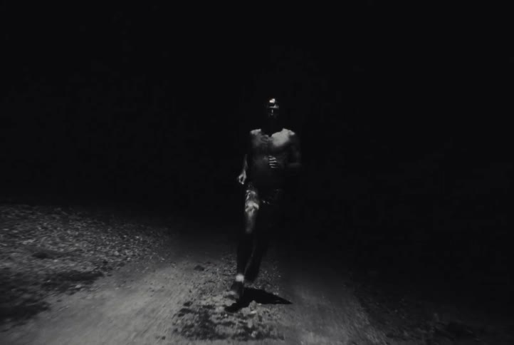 Bare chested man runs on a dirt road at night