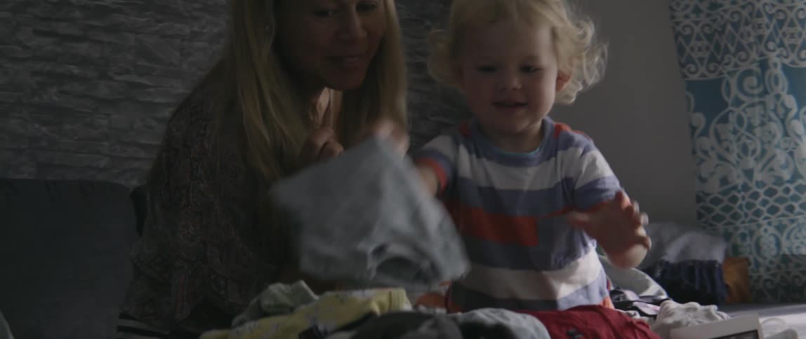 A young boy holds up laundry with his smiling mother nearby