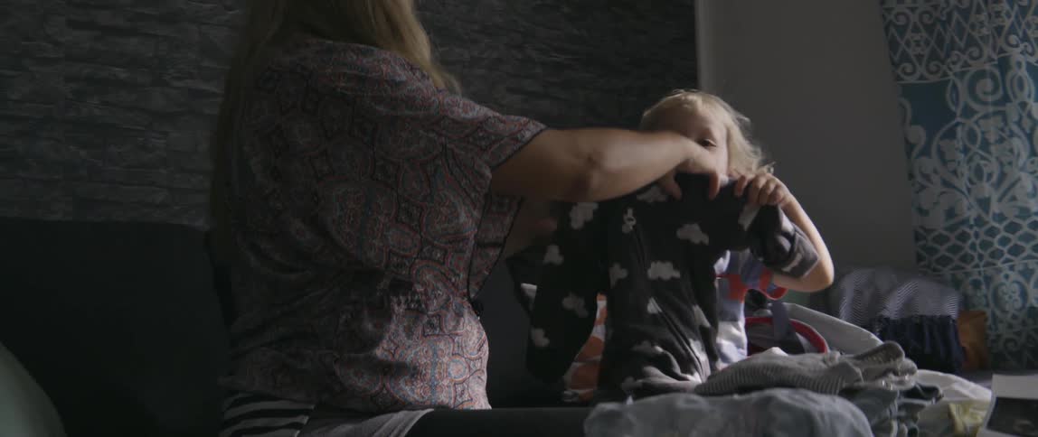 Toddler boy holding up his pajamas next to his mother in living room