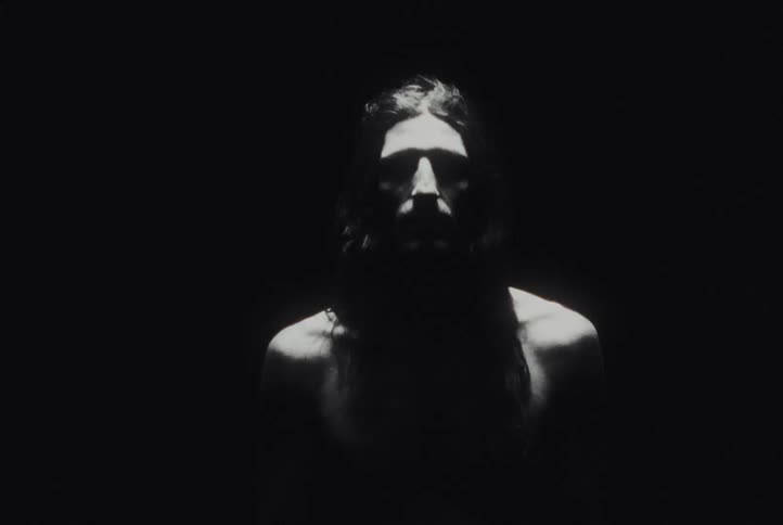 Shirtless person looks upward against a dark background