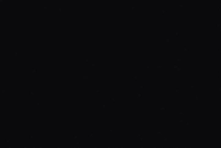 A dimly lit figure in flashing light emerges from deep shadows their face and shoulders faintly illuminated against a black background