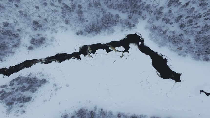 Unfrozen portion of a river flows through a snowy forest on a winter day