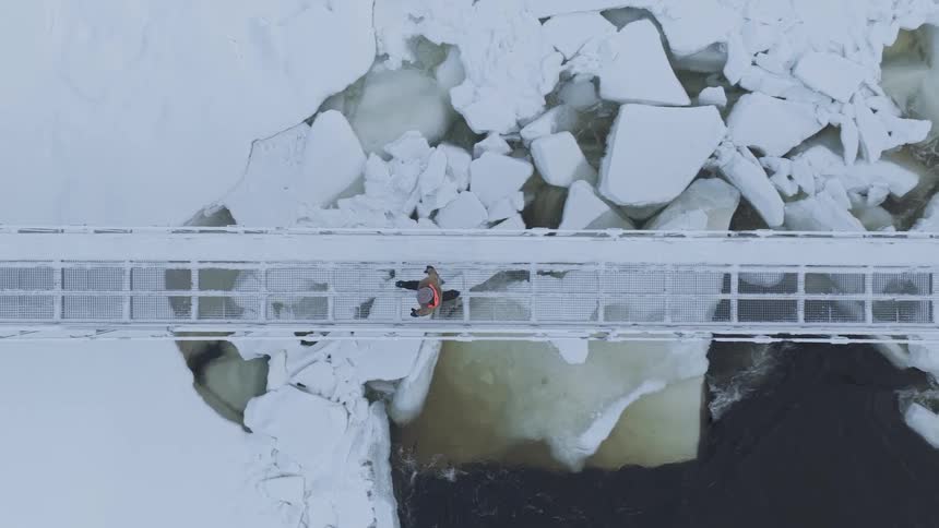 Hiker walking across a footbridge over an icy river