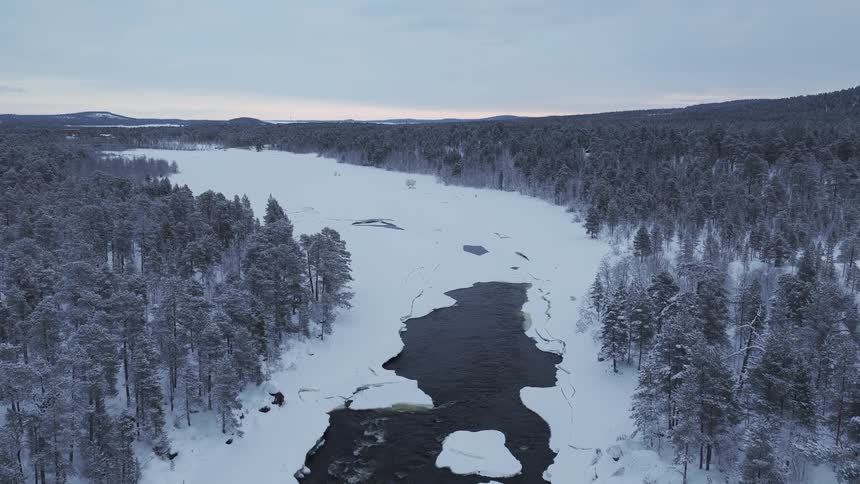 Ice covered river through the forest with forested mountains in the distance