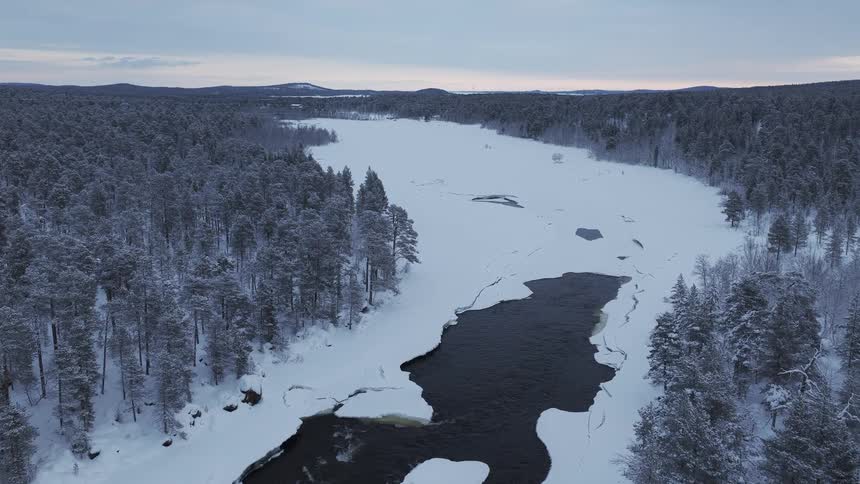 A wide frozen river winding through a dense snow covered pine forest under a gloomy winter sky