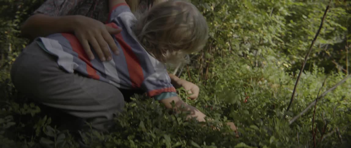 Happy mother and toddler boy enjoying a playful moment under trees in summer.