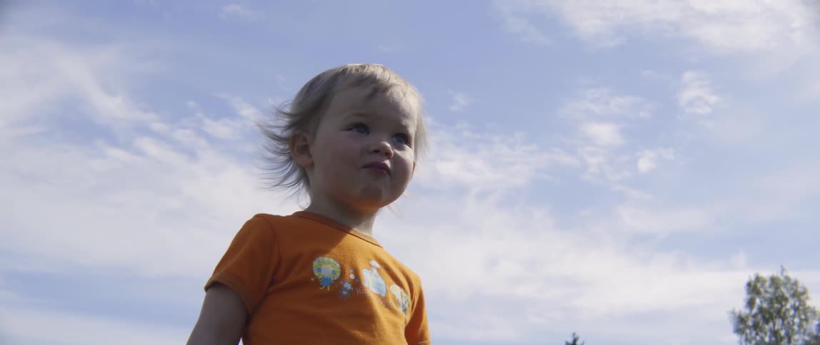 small child looking up with a curious expression outdoors during daytime.