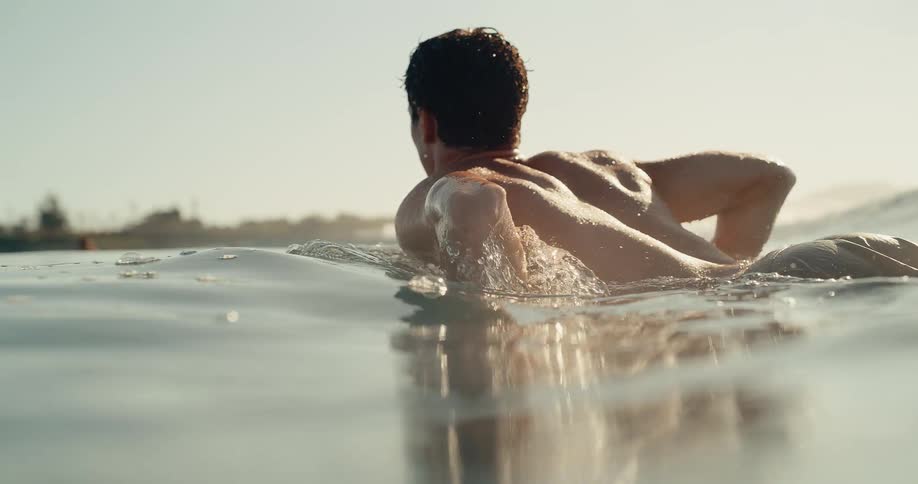 Male surfer swims while lying on his board on a sunny summer day