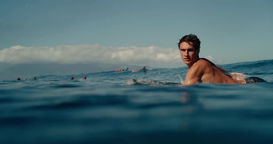 Man lying on a surfboard paddling in water off the coast among other people