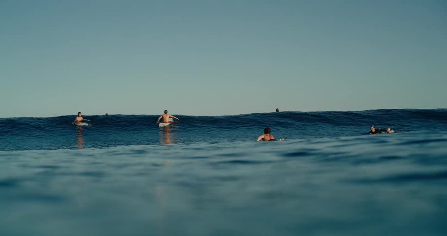 Surfers gently floating on surfboards beyond calm waves in the open ocean beneath a clear blue sky