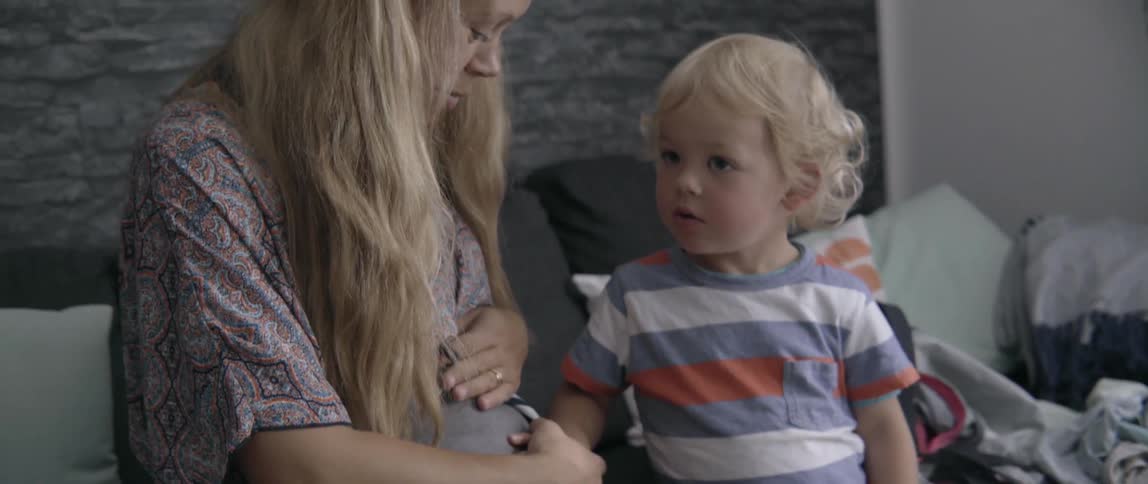 Pregnant mother and toddler boy bonding while touching her belly in a sunny home