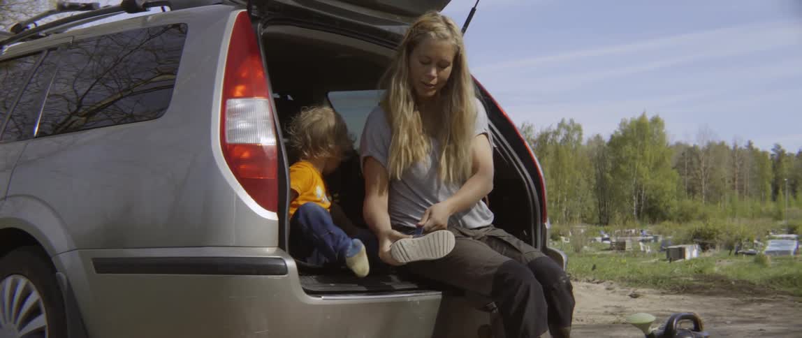 A woman puts on a toddler's shoes while sitting in the back of an open suv