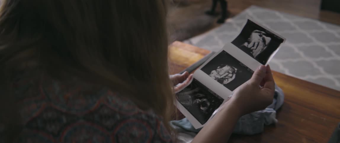 Woman sitting on a sofa while looking at baby ultrasound photos in the sun.