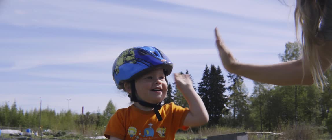 Woman high-fiving her child that's sitting on a bicycle on a cloudy day