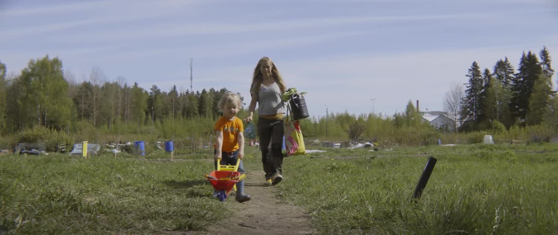 Woman walking outside with little boy who is pushing a toy wheelbarrow