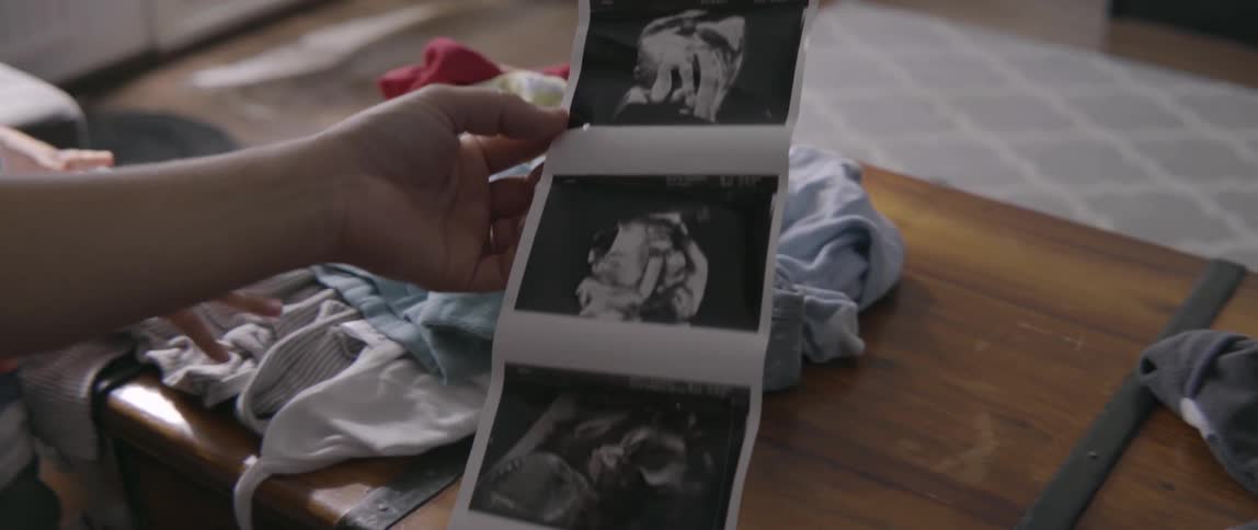 Woman holding sonogram pictures of unborn baby in living room