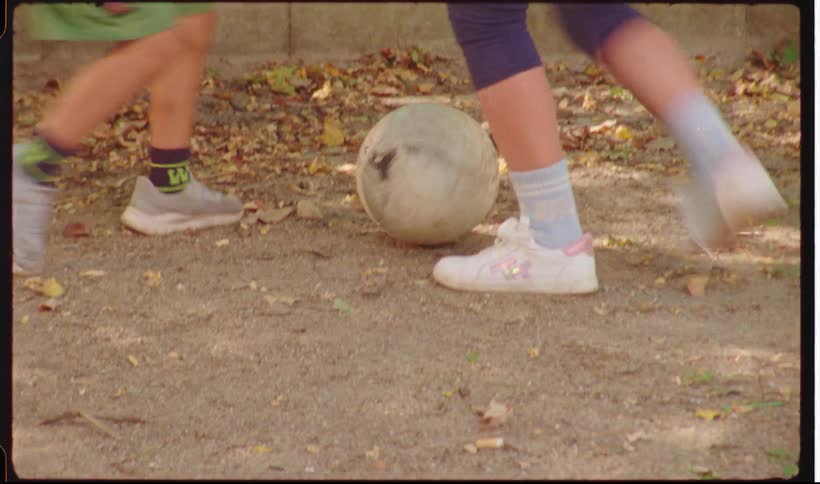 Three youngsters play with a soccer ball outdoors in a dirt yard