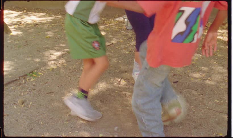 Four children play with a soccer ball in a park area with dirt and leaves on the ground