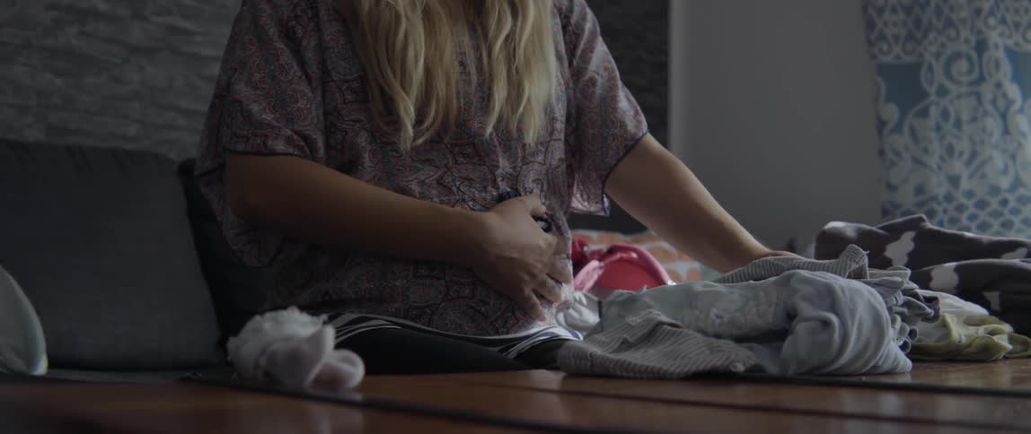 Woman performing domestic household chores while folding clothes on a bed in the morning.