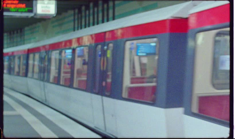 A modern white subway train with a distinct red stripe and blue accents pulls into a station the footage is presented in a grainy vintage film aesthetic and features a large watermark across the center of the frame