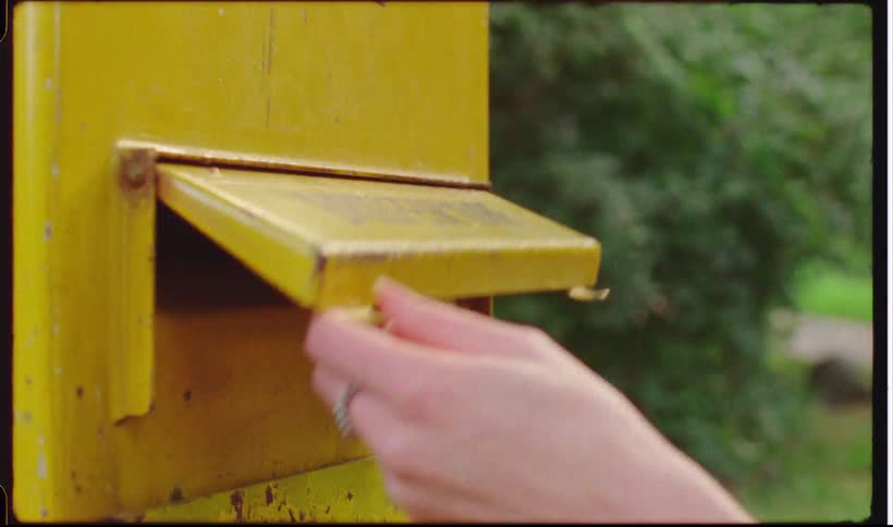 A person inserts an envelope into a yellow public mailbox