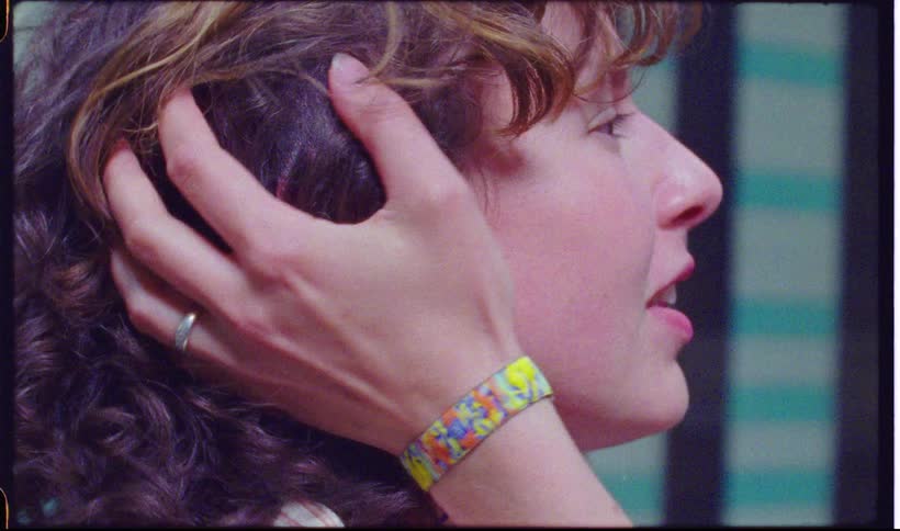 A hand wearing a bracelet and ring is stroking the hair of a smiling curly haired profile of a person