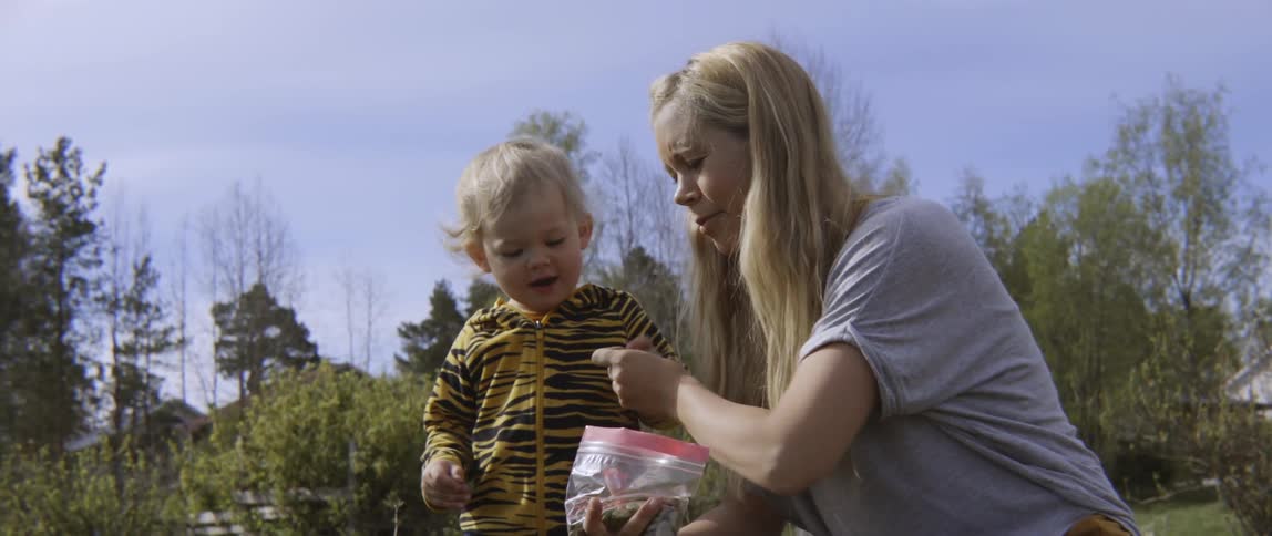 Mother gives toddler boy seeds from a bag to plant outside on sunny day