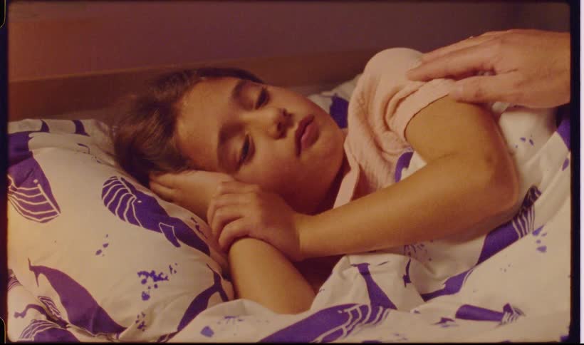Child sleeping in bed while a hand touches her shoulder