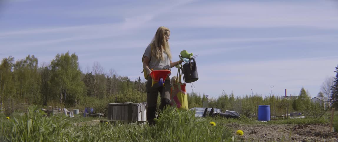 Woman carrying several things with her child following closely behind in a field on a cloudy day