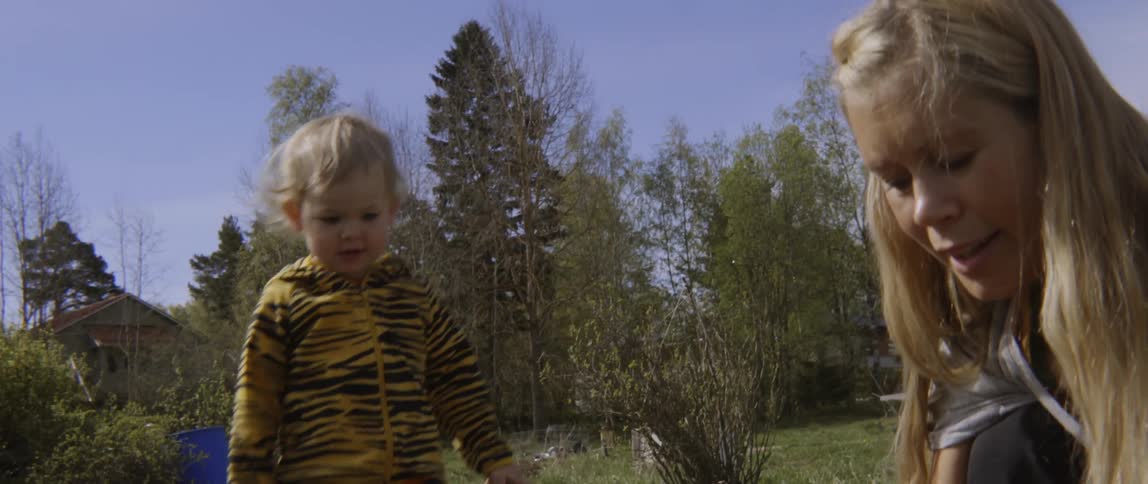 Toddler boy walks to his mother who is working in garden on sunny day