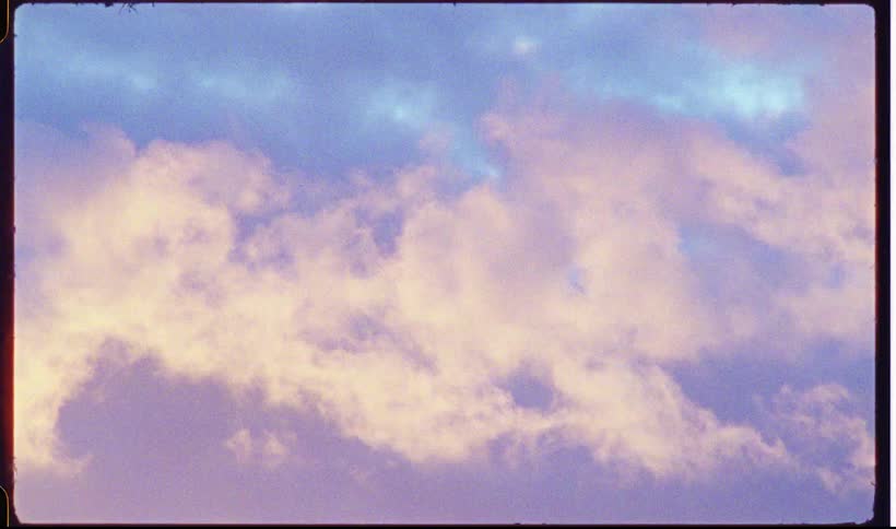 Dark purple and blue clouds drift across a sunset sky while the silhouettes of houses and trees sit along the bottom of the frame during the final moments of daylight in a quiet neighborhood