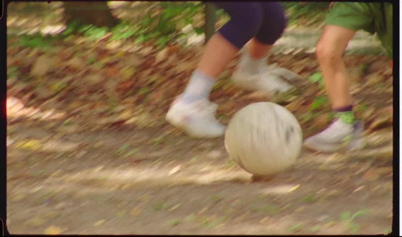 Kids play with a soccer ball on a dirt field during the daytime