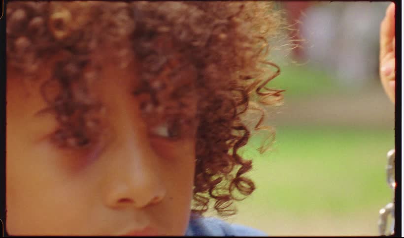 A close up of a black child looking sad holding onto a silver large chain outdoors
