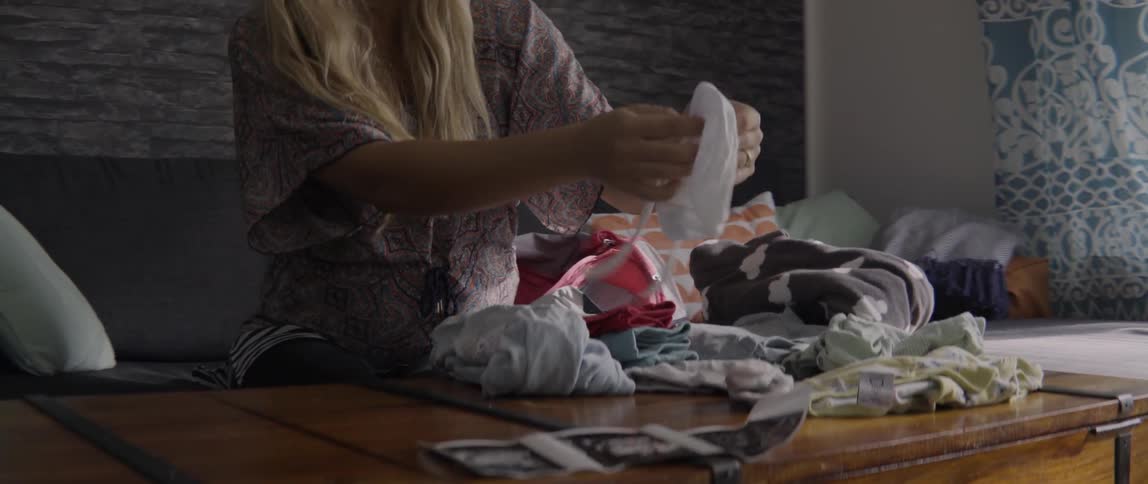Woman performing domestic household chores while folding clean laundry in a bright living space.