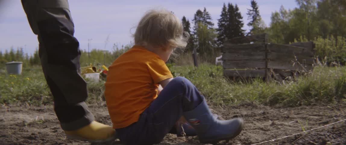 A toddler boy standing up from the ground with his mother helping him.